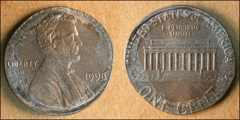 1998 Lincoln penny struck on dime planchet appearing silver-colored and smaller than normal, shown next to a regular 1998 penny for comparison